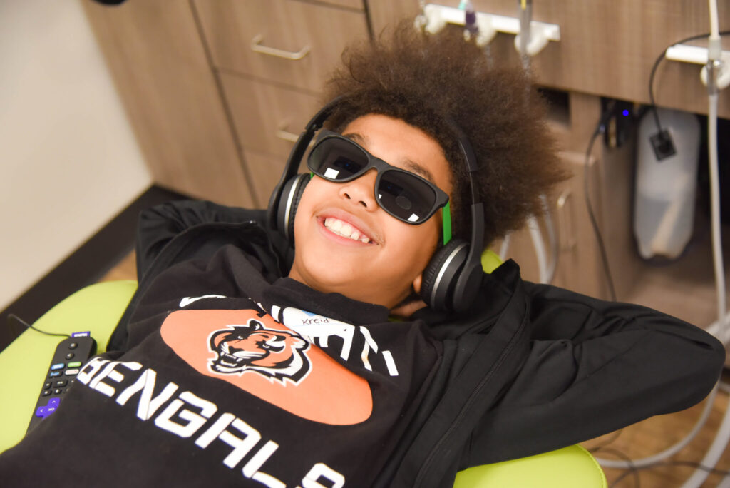 Boy in an exam chair smiling listening to music.