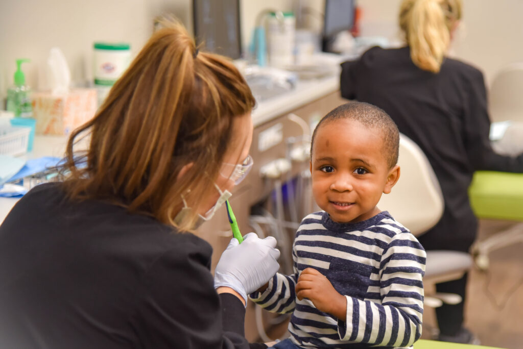 A photo of a young boy with a Spring Creek Pediatric team member smiling and learning how to use a toothbrush.